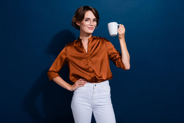 漂亮的年轻女孩的照片肖像拿着咖啡杯喝酒穿着时髦的棕色衬衫孤立在深棕色的背景图片下载