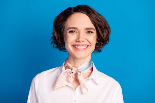 照片迷人的女士灿烂的微笑，看相机系在脖子上围巾孤立的蓝色背景图片下载