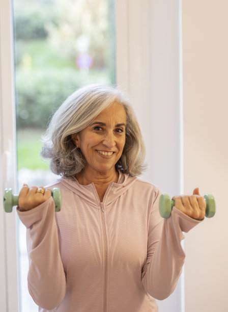 这是一位退休的老年妇女在拿着哑铃进行康复训练时看着相机的照片图片下载