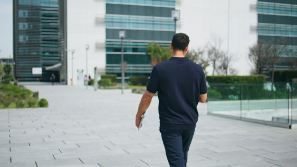 悠闲的男子漫步广场后景。悠闲的商人漫步在阳光明媚的城市图片下载