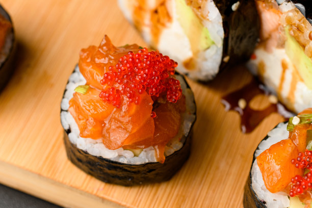 特写照片卷鲑鱼，tobiko小牛包裹在海苔在木制砧板上图片下载