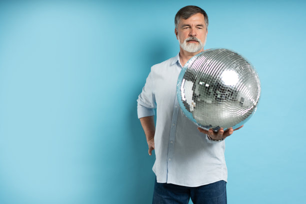 照片正面老人拿迪斯科球孤立在蓝色背景。图片下载