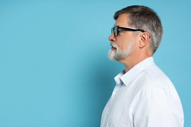 侧面特写照片成功成熟英俊的深褐色胡子商人在正式的服装和黑色眼镜在纯蓝色的背景。图片下载