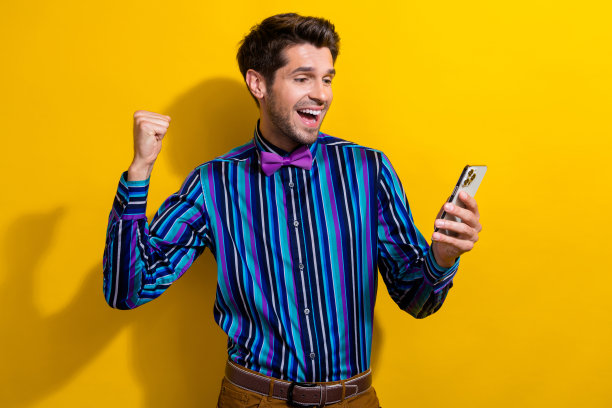 照片中，一个穿着条纹衬衫、打领带、拿着智能手机、拿着彩票的欣喜若狂的男人被隔离在鲜艳的黄色背景上图片下载