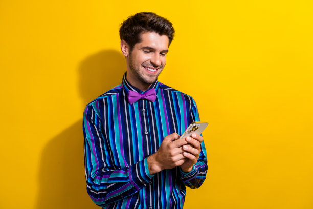 照片的聪明聪明的绅士穿着条纹衬衫领带蝴蝶结阅读电子邮件的智能手机孤立在鲜艳的黄色背景图片下载