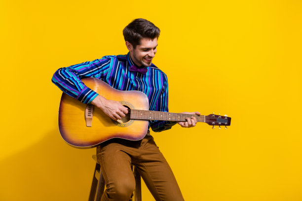 照片好心情的人与胡茬穿着条纹衬衫学习吉他上孤立的黄色背景图片下载