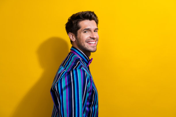 侧面侧面照片，乐观的家伙留着胡茬，穿着条纹衬衫，在黄色背景上对着相机微笑图片下载