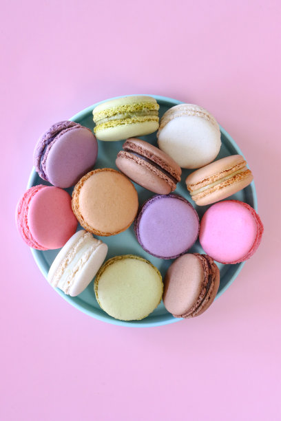 彩色马卡龙的图片，里面装满了黄油奶油、草莓、香草、蓝莓、橘子、开心果、巧克力味的蛋白霜，粉红色的背景，高架视图图片下载