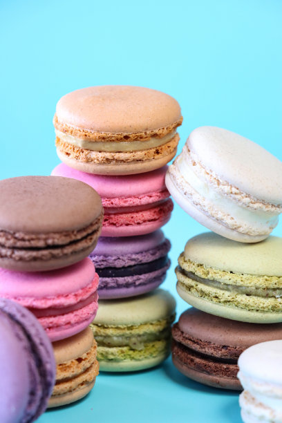 五堆马卡龙的特写图片，五颜六色的马卡龙填充了调味奶油，开心果，蓝莓，草莓，咖啡，开心果，香草味蛋白霜，蓝色背景，重点在前景图片下载