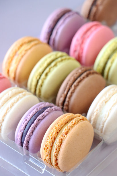 特写图片:一排排五颜六色的马卡龙，在一次性塑料托盘里装满了各种口味的白脱奶油，草莓、香草、蓝莓、橘子、开心果、巧克力口味的蛋白霜，紫色的背景，突出的前景图片下载