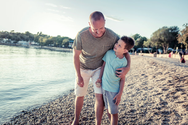这是一对父子在户外享受一天的照片。一个年轻人和他的儿子沿着海滩散步的镜头。图片下载