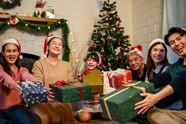 亚洲家庭在家里交换圣诞礼物的照片。迷人快乐的人们拿着礼品盒，一起在客厅里庆祝节日感恩节、平安夜的传统。图片下载