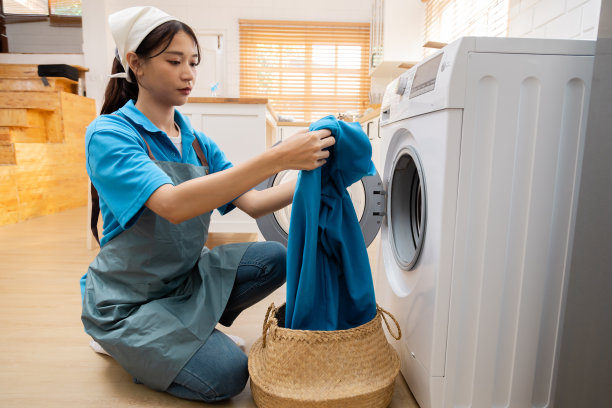 亚洲女佣在服务公司的团队工作，在客户的房子清洁，洗衣坐在厨房用洗衣机洗衣服，家庭主妇工作穿着围裙保健服白色面料图片下载