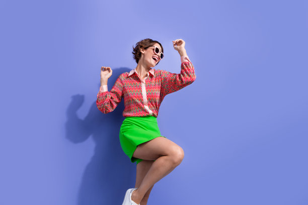 照片华丽的女人与鲍勃发型穿着印花衬衫在眼镜跳舞享受迪斯科派对孤立的蓝色背景图片下载