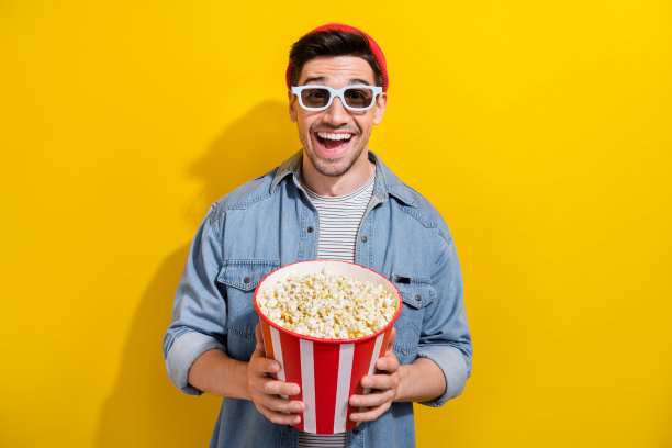 照片印象深刻的积极的家伙穿牛仔夹克看vr电影吃爆米花孤立的黄色背景图片下载