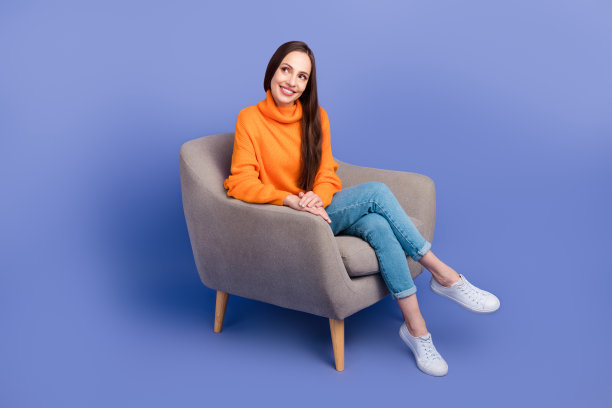 开朗的女士在灰色扶手椅上坐着的全身照片放松地看着空旷的空间好奇的折扣孤立在紫色的背景上图片下载