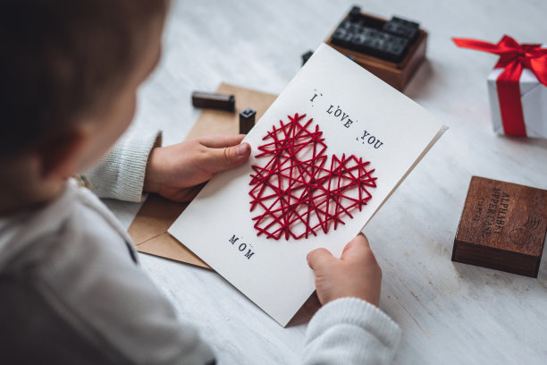 儿童工艺的概念，母亲节的手工礼物。小男孩手里拿着绣着心形的手工卡片，上面印有“我爱你，妈妈”的字样。儿童休闲活动，手工艺品图片下载