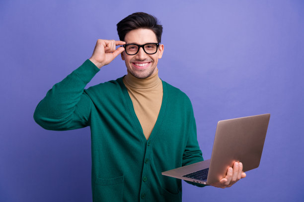 照片中自信迷人的男人穿着时尚的绿色衣服，戴着眼镜，现代设备上网本孤立在紫色的背景图片下载