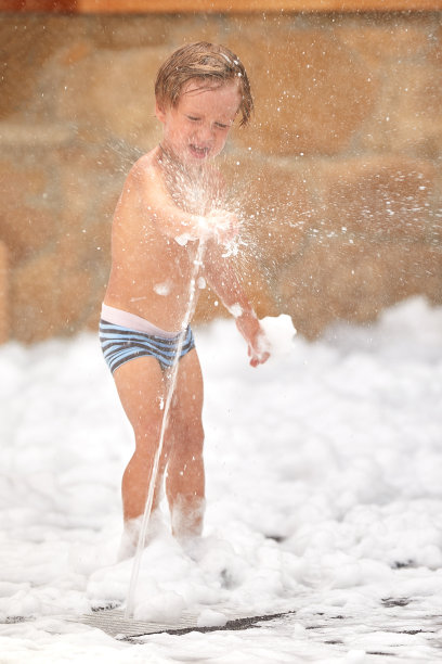 小男孩在水龙头下参加水上乐园期间的泡沫派对，户外水上游戏，孩子们的快乐图片下载