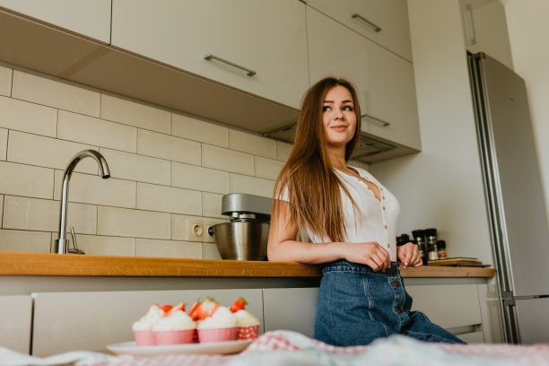 友善微笑的女性专业糖果师用糕点袋给纸杯蛋糕浇上奶油的照片。看着镜头。在室内的形象。做奶油蛋糕的女糕点师图片下载