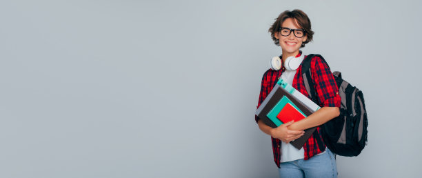 横幅广告照片可爱的微笑的年轻女学生戴着眼镜，背包和书在灰色背景下摆姿势。大学，学习，学校，教育，学院，班级，知识。图片下载