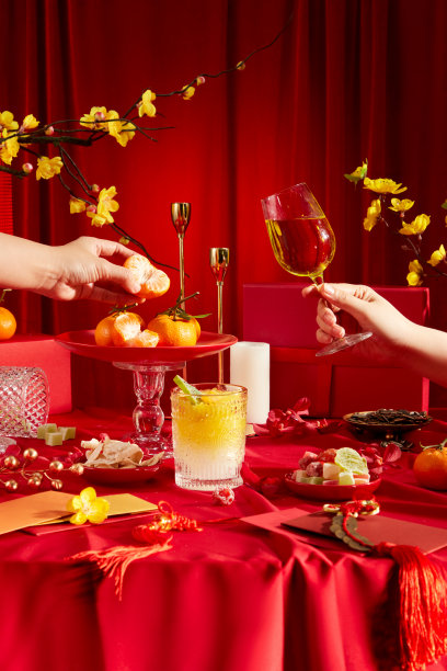 春节聚会桌的正面视图，背景为亮红色。现场有装饰品，黄杏花，果酱，酒，橘子，红包和礼品盒。广告。图片下载