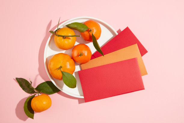 粉色背景上的三个红包和一盘橘子的俯视图。有特色的春节广告文案空间。图片下载