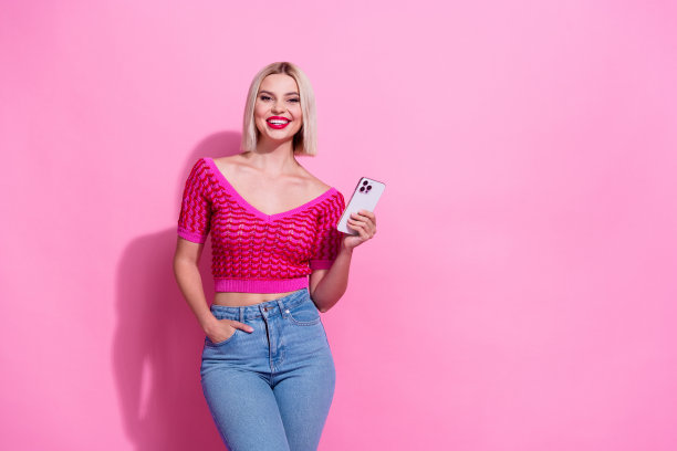 照片中，开朗可爱的短发女子穿着针织衫，将智能手机的手臂放在口袋里，孤立在粉红色的背景下图片下载