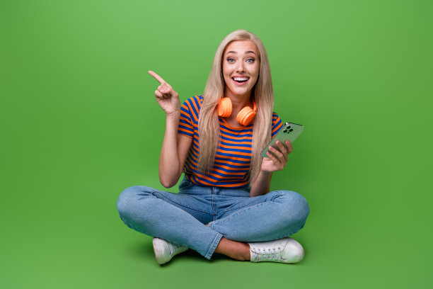 照片年轻的金发白人妇女享受听音乐蓝牙耳机点手指网站孤立的绿色背景图片下载