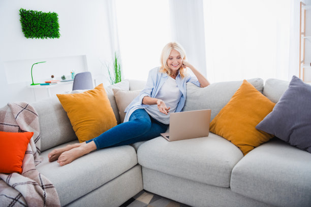 照片肖像迷人的退休妇女坐在沙发沟通视频通话上网本周末时尚的家居装饰客厅现代的公寓图片下载