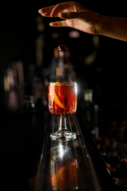 吧台上，酒保的手把小樱桃干扔进透明的玻璃杯里，里面装着美味的酒精饮料图片下载