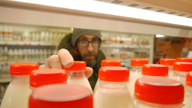 超市里许多红色瓶盖的牛奶瓶的特写，一位男顾客拿着一瓶图片下载