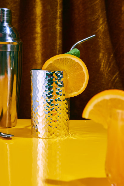 酒精饮料的特写照片，鸡尾酒在银色玻璃杯装饰着一块水果，橙色站在黄色的吧台上。节日心情的概念。图片下载