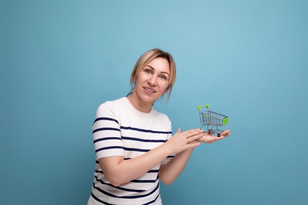 年轻可爱的休闲购物狂手持超市购物车的横向照片，蓝色背景与复制空间图片下载