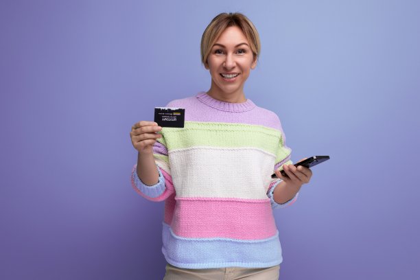 穿着浅色条纹毛衣的年轻金发女子微笑着拿着一张紫色背景的信用卡图片下载