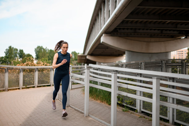 在桥附近的城市街道上慢跑的年轻运动女子的正面照片图片下载