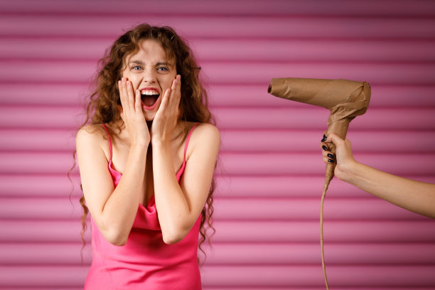 年轻的积极微笑的女人收到惊喜的礼物手持电吹风包裹在质朴的米色工艺纸包。黑色星期五概念图片下载