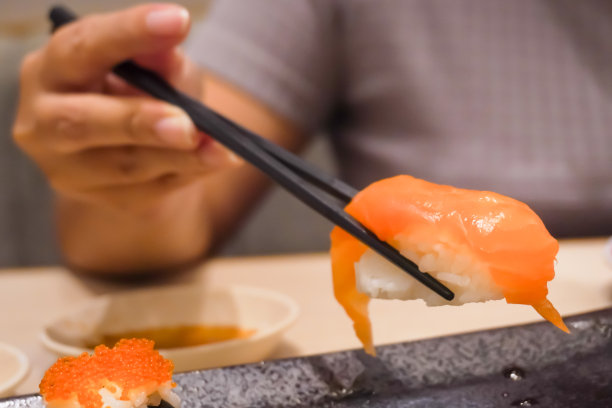 在日本餐厅，有人用筷子吃鲑鱼寿司的特写照片。整体健康食品，营养，欧米茄-3，动物蛋白，海鲜，现代恢复和街头食品的概念。图片下载