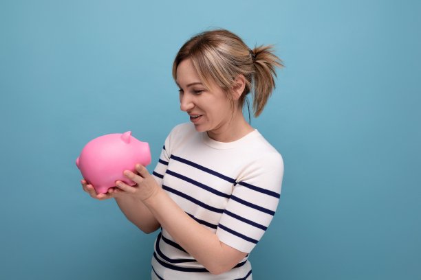 一个迷人的年轻女子的横向照片，在一个蓝色的背景与复制空间，在休闲服装与硬币的小猪存钱罐图片下载