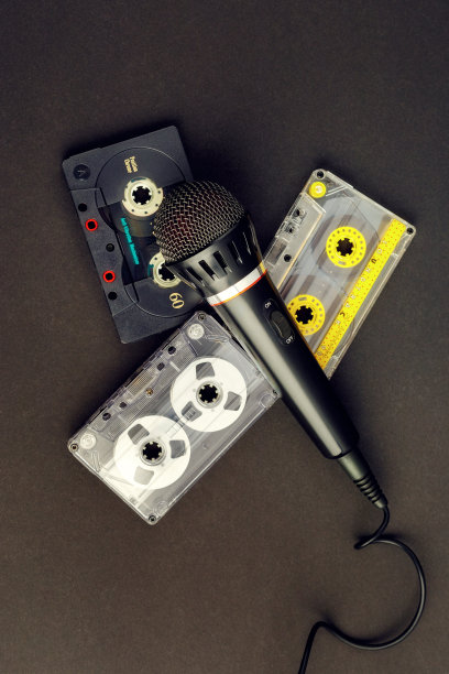 黑色专业卡拉ok麦克风和三个彩色复古录音带在黑色的背景。80年代模拟音频设备的垂直照片图片下载