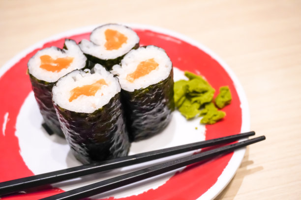 在日本餐厅，有人用筷子吃三文鱼寿司卷的特写照片。整体健康食品，营养，欧米茄-3，动物蛋白，海鲜，现代恢复和街头食品的概念。图片下载