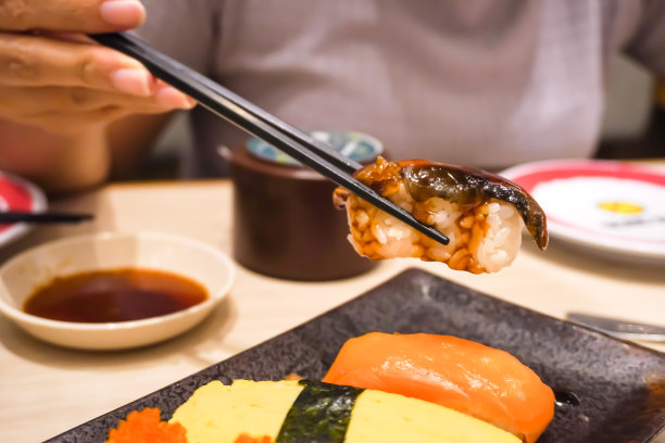 在日本餐厅，有人用筷子吃寿司的特写照片。整体健康食品，营养，欧米茄-3，动物蛋白，海鲜，现代恢复和街头食品的概念。图片下载