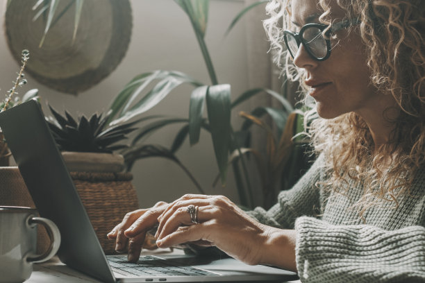 一个女人在家里使用笔记本电脑在绿色的情绪色背景和环境。房子的室内花园为背景。有魅力的女性用电脑工作或在室内休闲的生活方式上网图片下载