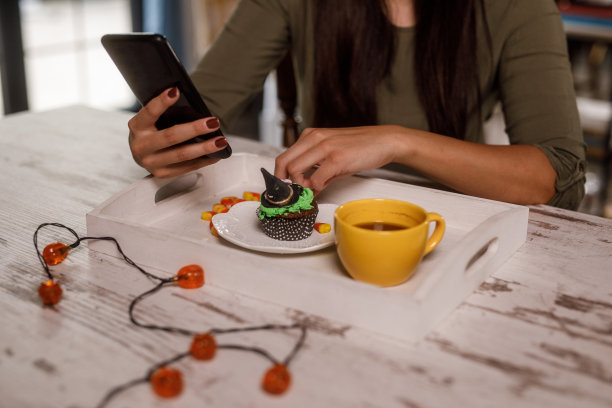 一边喝着咖啡，吃着万圣节纸杯蛋糕，一边用智能手机上网图片下载