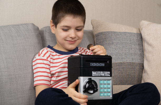 一个小男孩把一枚硬币放进了一个安全的储蓄罐。为孩子们提供金融知识。图片下载