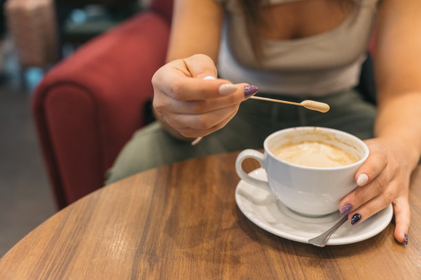 不知名的女人在品尝甜咖啡的泡沫。一个匿名的年轻女孩从她的咖啡中取出现煮的泡沫来品尝它的特写图片。图片下载