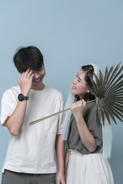 亚洲年轻夫妇穿休闲装，新娘戴面纱。幸福和享受照片一起在工作室浅蓝色背景。图片下载