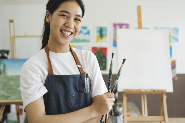 年轻的亚洲女艺术家在艺术工作室看着相机，微笑着。图片下载