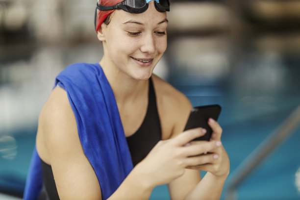 一名专业游泳女孩在泳池附近使用手机的照片。图片下载