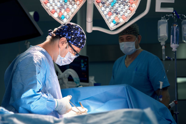 The doctor performs an operation in a dark operating room with a lamp in the background, a professional surgeon during a stressful operation.图片下载